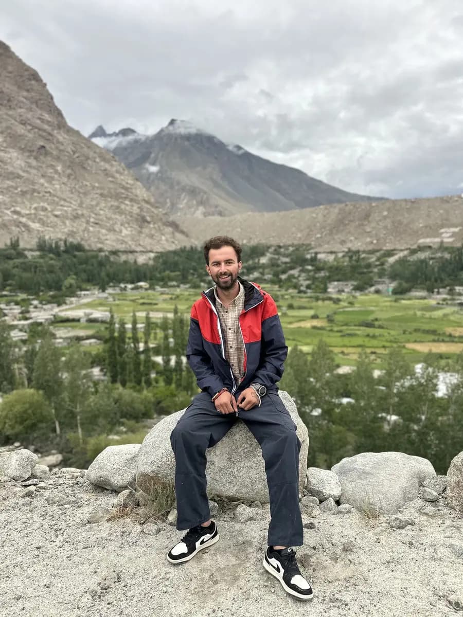 Ali, a Ghulkin-born trekking guide, sitting on a boulder above the village with the Karakoram behind him